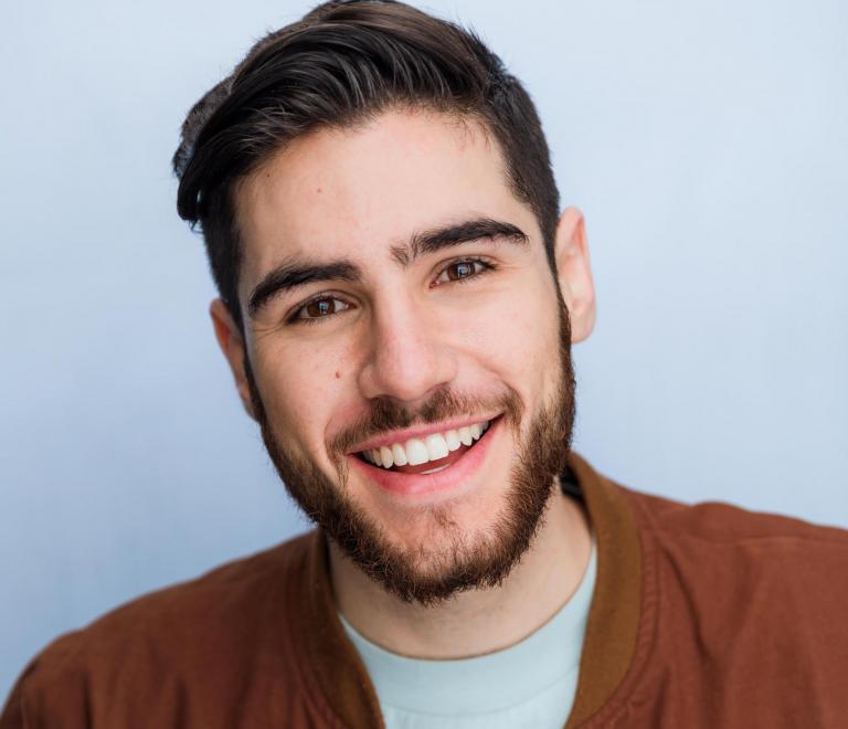 headshot of comedian Sam Morrison, a white male with beard, brown jacket, light blue tshirt 